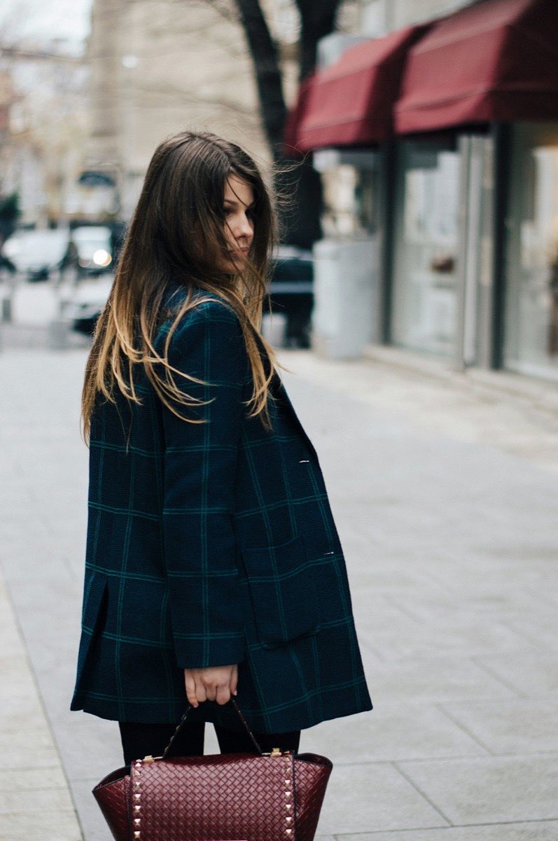 Woman in a dark plaid coat walking along a city sidewalk
